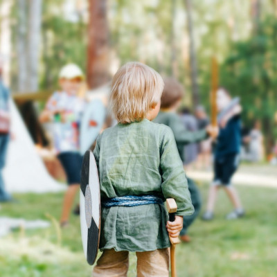 Viking game for kids. Rear view of little boy in medieval clothes holding wooden toy shield